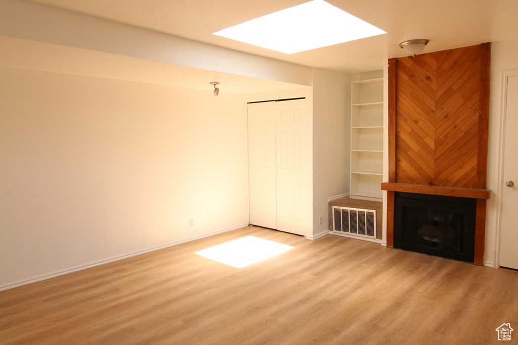 Unfurnished living room featuring a large fireplace, baseboards, visible vents, and wood finished floors