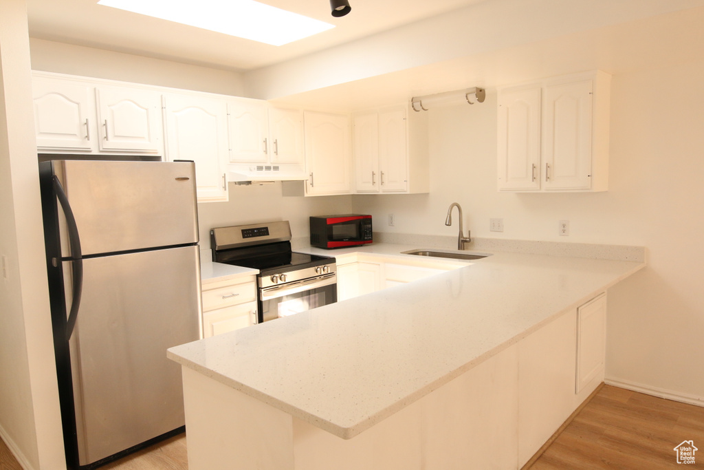 Kitchen featuring a peninsula, a sink, stainless steel appliances, white cabinetry, and light wood-type flooring