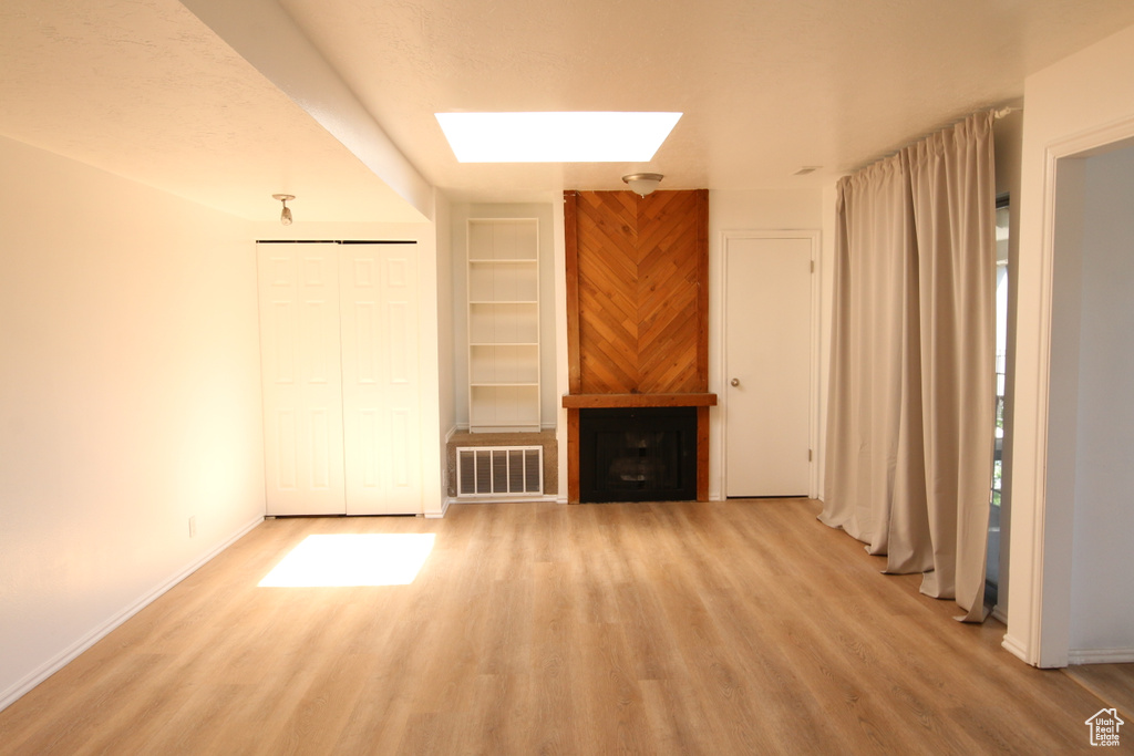 Unfurnished living room with light wood-type flooring, visible vents, and a skylight