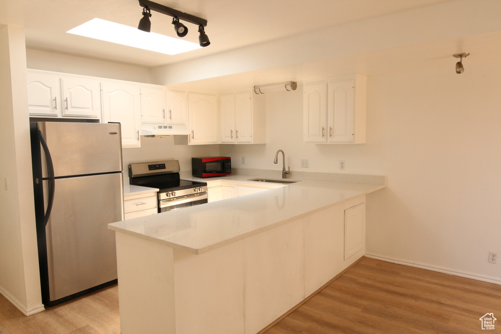 Kitchen featuring a sink, a peninsula, under cabinet range hood, white cabinetry, and appliances with stainless steel finishes