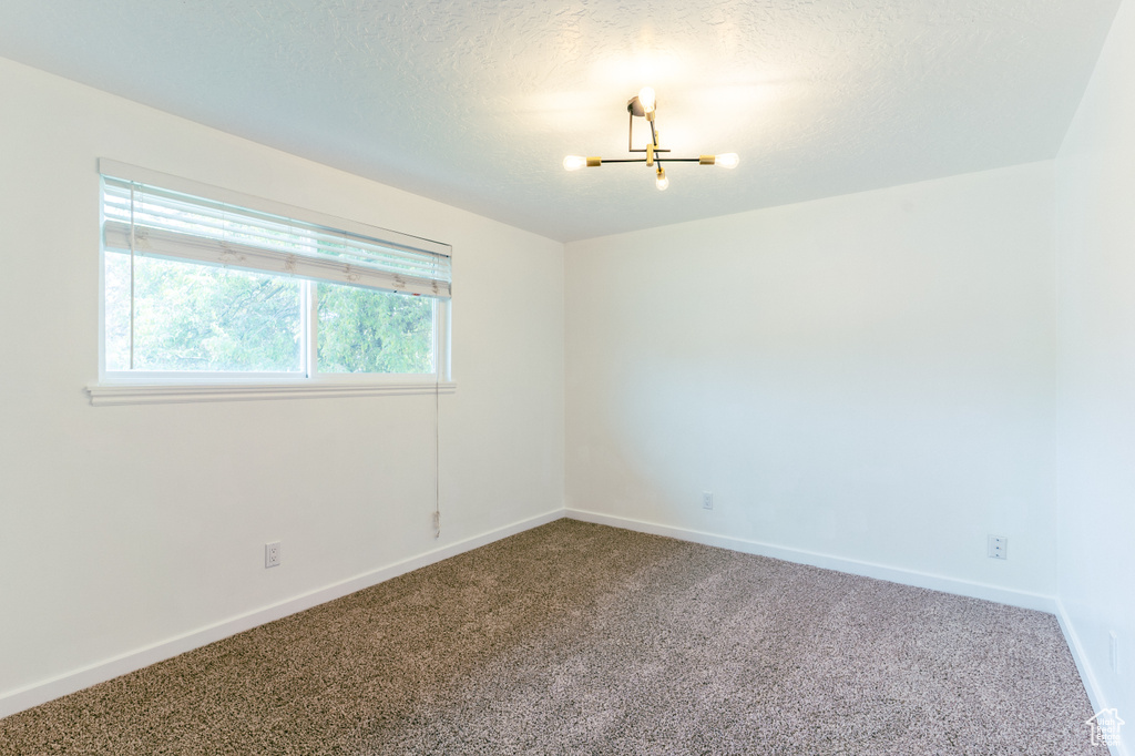 Spare room featuring baseboards, a textured ceiling, a chandelier, and carpet