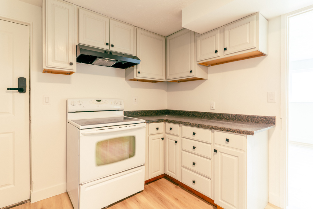 Kitchen with under cabinet range hood, dark countertops, white electric stove, and light wood-style floors