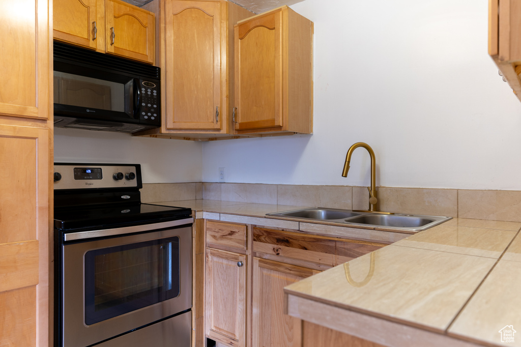 Kitchen featuring stainless steel electric range oven, black microwave, light countertops, and a sink