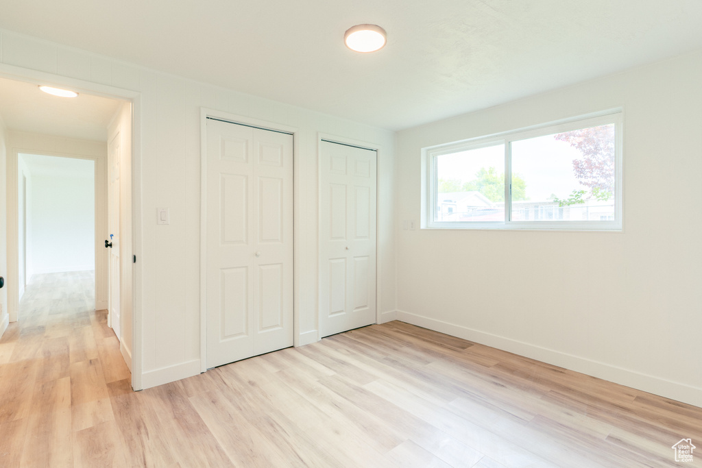 Unfurnished bedroom with baseboards, light wood-type flooring, and two closets