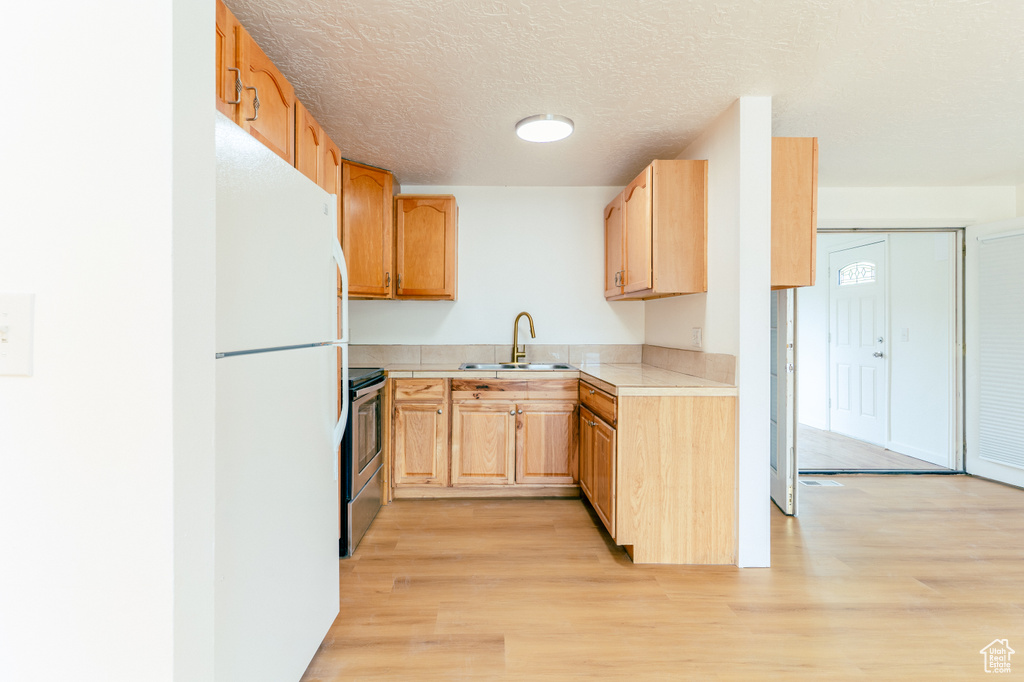Kitchen featuring a sink, freestanding refrigerator, stainless steel electric range, light countertops, and light wood-style floors