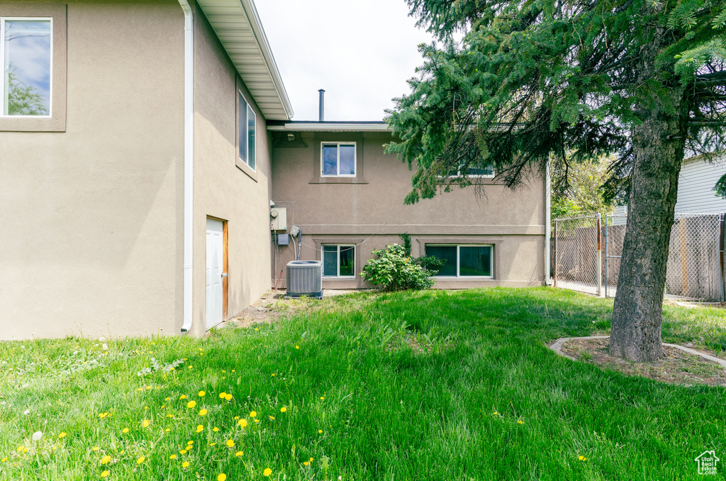 Back of house featuring a yard, stucco siding, fence, and central AC