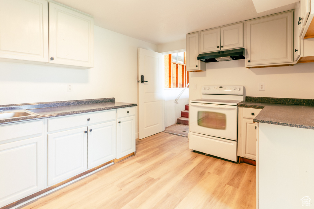 Kitchen with under cabinet range hood, white range with electric stovetop, dark countertops, and light wood-style floors