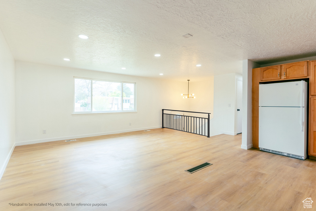 Unfurnished room with a chandelier, a textured ceiling, light wood finished floors, and recessed lighting