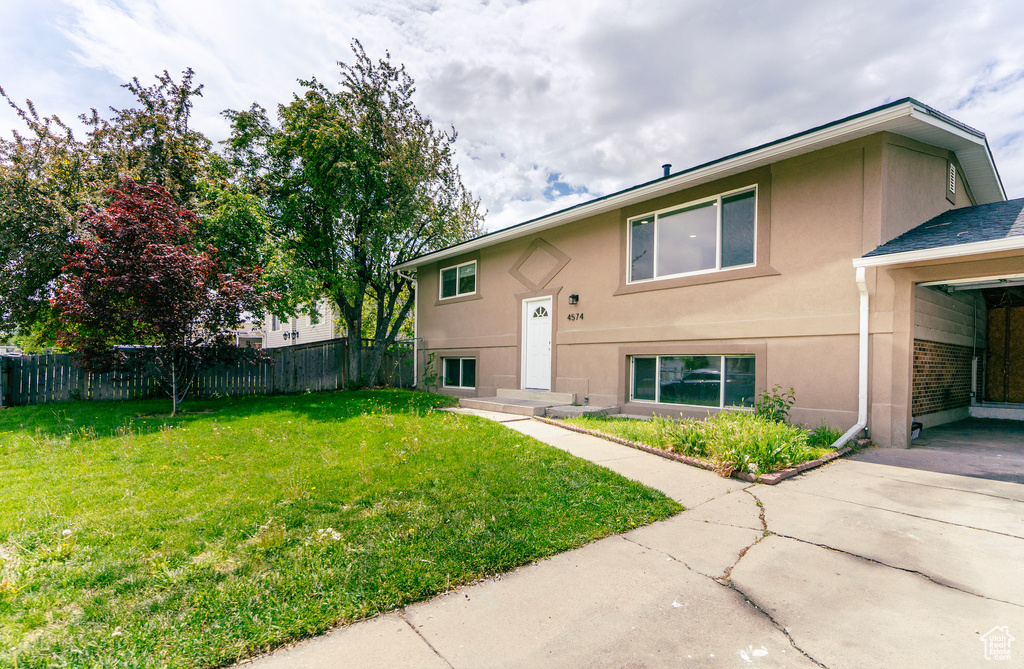 Back of house with fence, driveway, stucco siding, and a lawn