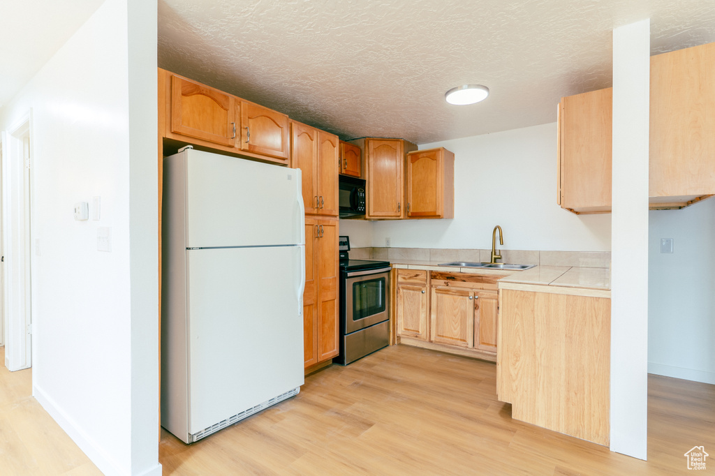 Kitchen with light wood finished floors, a sink, freestanding refrigerator, stainless steel electric stove, and black microwave