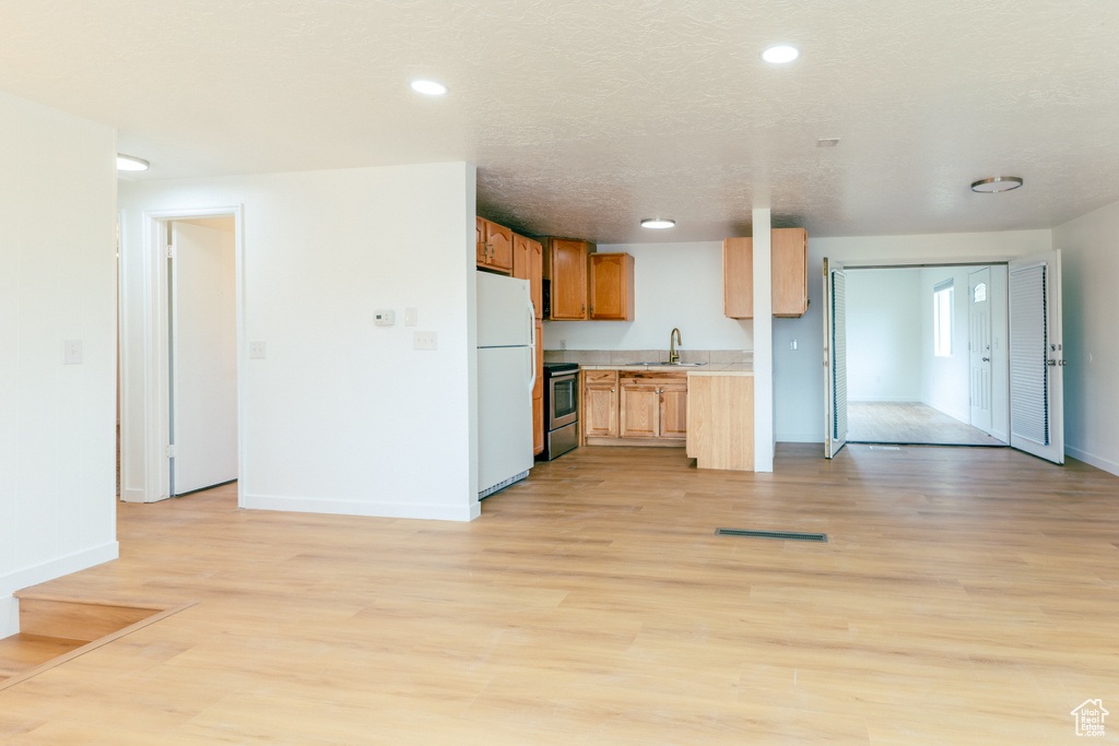 Kitchen featuring freestanding refrigerator, stainless steel electric range oven, a sink, open floor plan, and light countertops