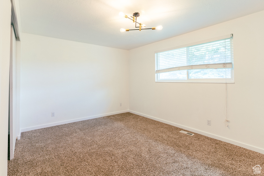 Carpeted empty room with visible vents, baseboards, and a notable chandelier