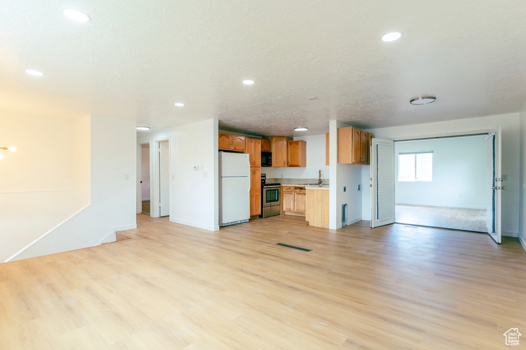 Kitchen featuring stainless steel electric stove, freestanding refrigerator, black microwave, open floor plan, and light countertops