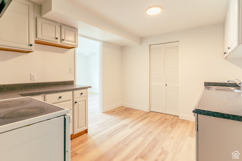 Kitchen featuring a sink, light wood-style flooring, white electric range oven, baseboards, and dark countertops