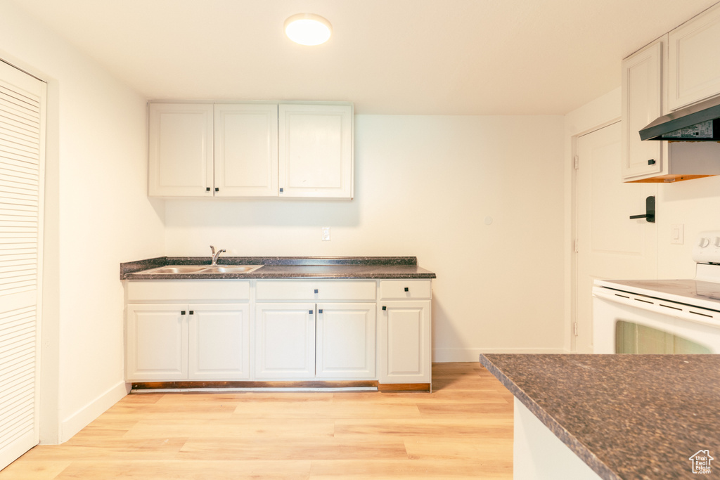 Kitchen featuring a sink, light wood-style flooring, dark countertops, and electric range