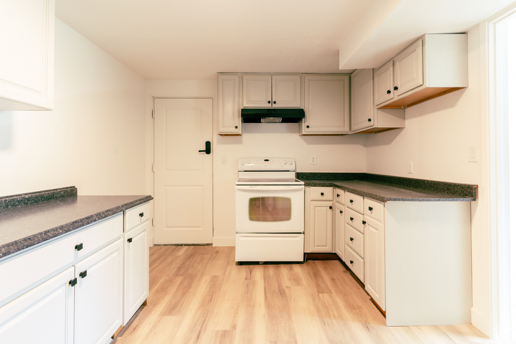 Kitchen with white electric range oven, dark countertops, under cabinet range hood, and light wood finished floors