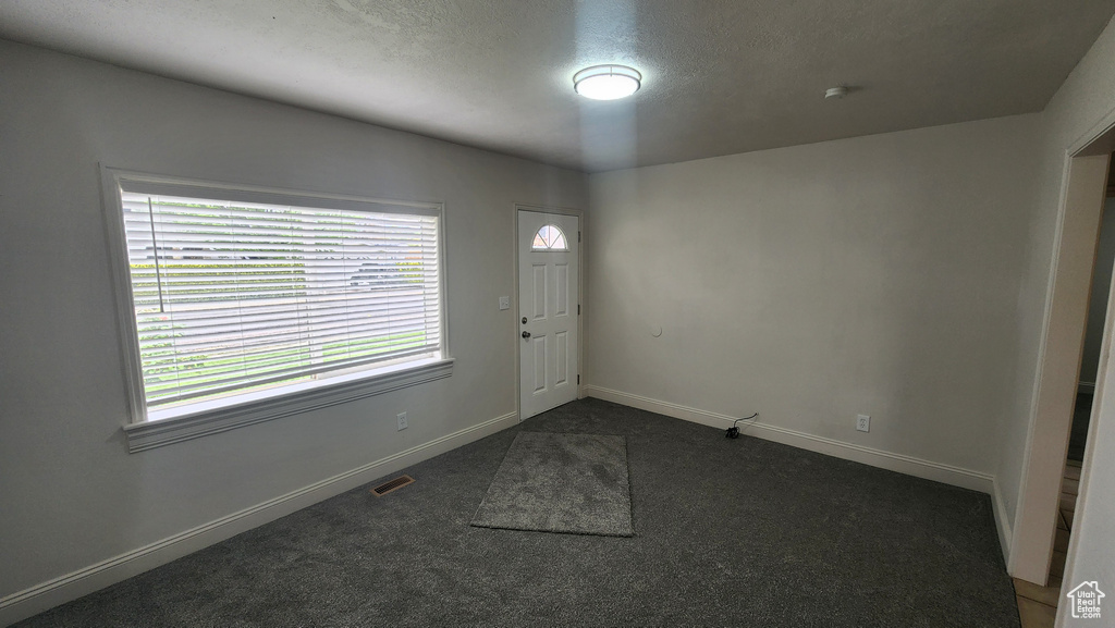 Foyer entrance featuring a textured ceiling, baseboards, visible vents, and dark carpet