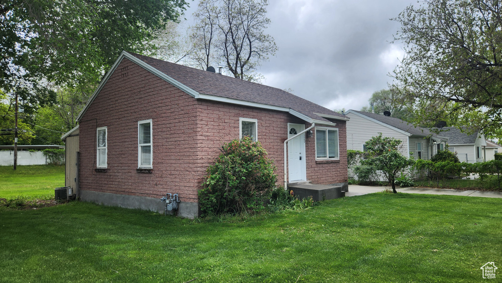 View of property exterior featuring a yard, central air condition unit, and brick siding