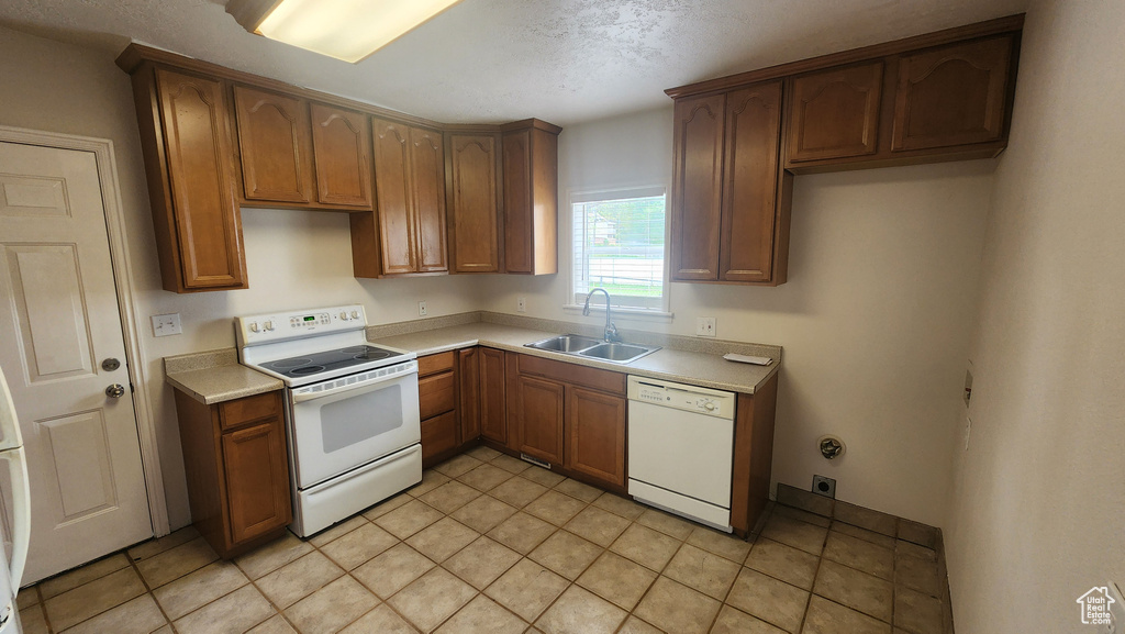 Kitchen with light countertops, brown cabinetry, a sink, and white appliances