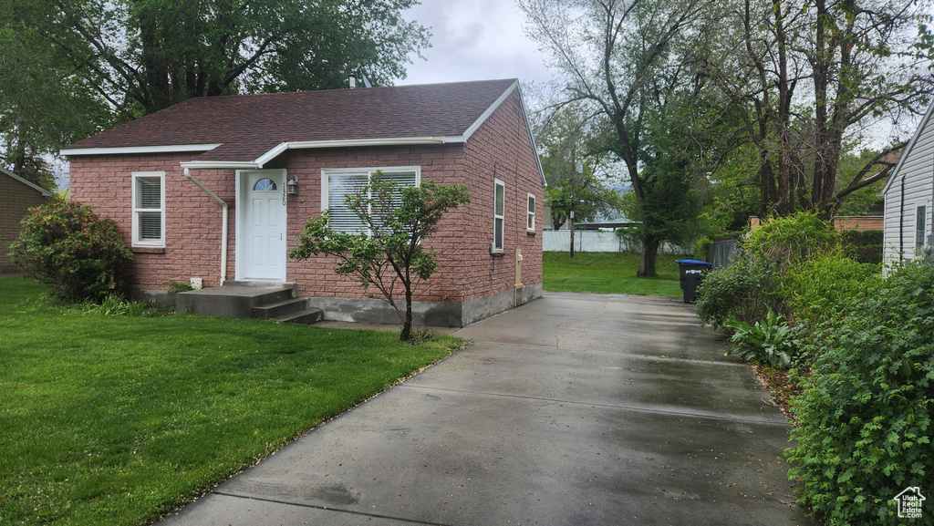 Bungalow featuring concrete driveway, a front yard, roof with shingles, and brick siding