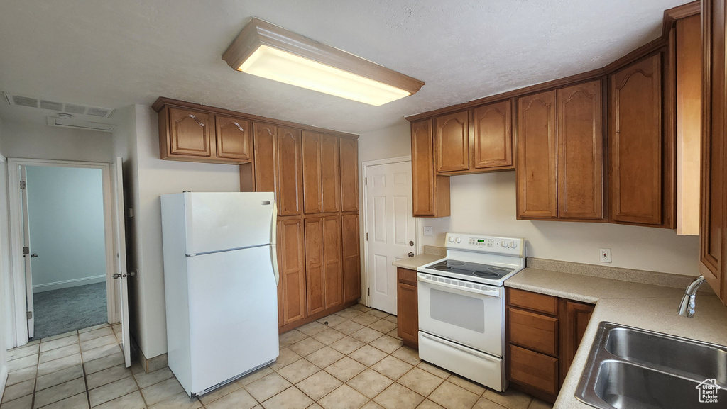 Kitchen with light tile patterned floors, a sink, visible vents, white appliances, and light countertops