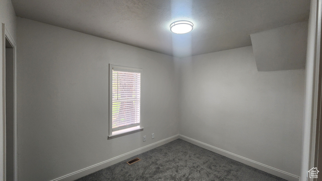 Spare room with visible vents, baseboards, and dark carpet