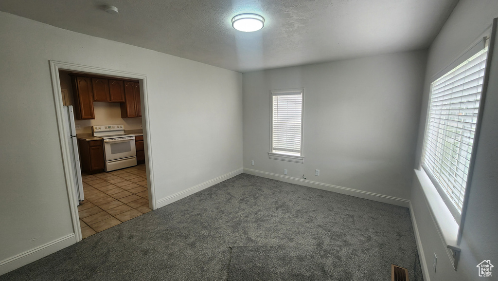 Empty room with a textured ceiling, baseboards, light tile patterned floors, visible vents, and light carpet