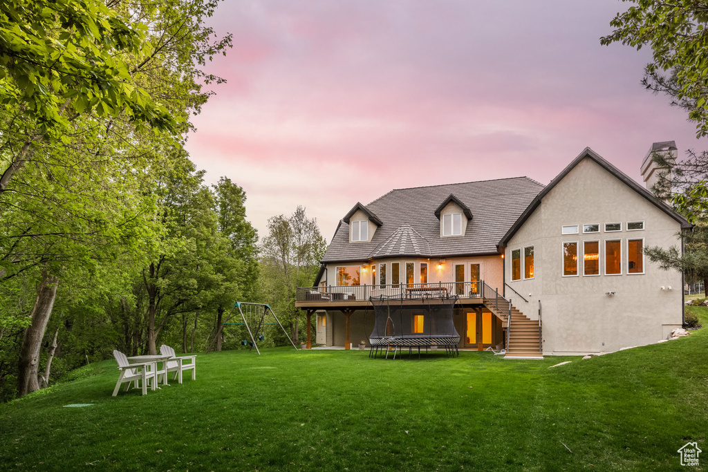 Back of house at dusk featuring a deck, stairs, a yard, stucco siding, and a chimney