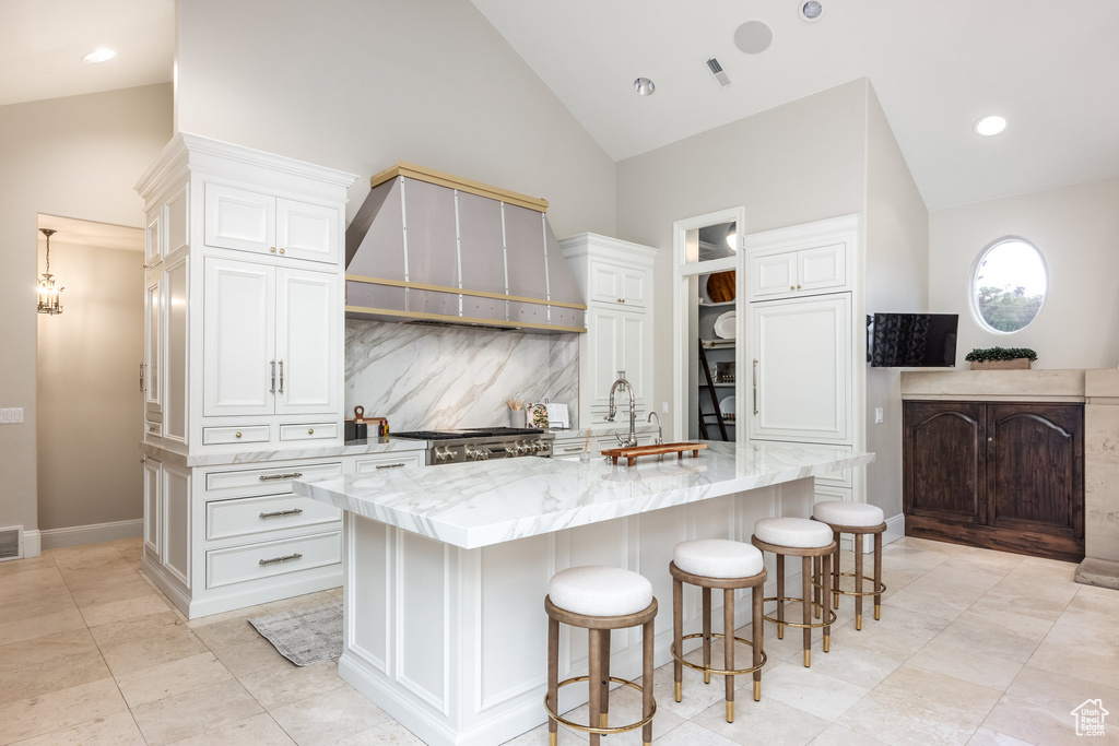 Kitchen with light stone countertops, decorative backsplash, custom range hood, and white cabinets