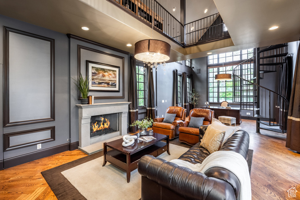 Living area featuring wood finished floors, stairway, a lit fireplace, and a towering ceiling