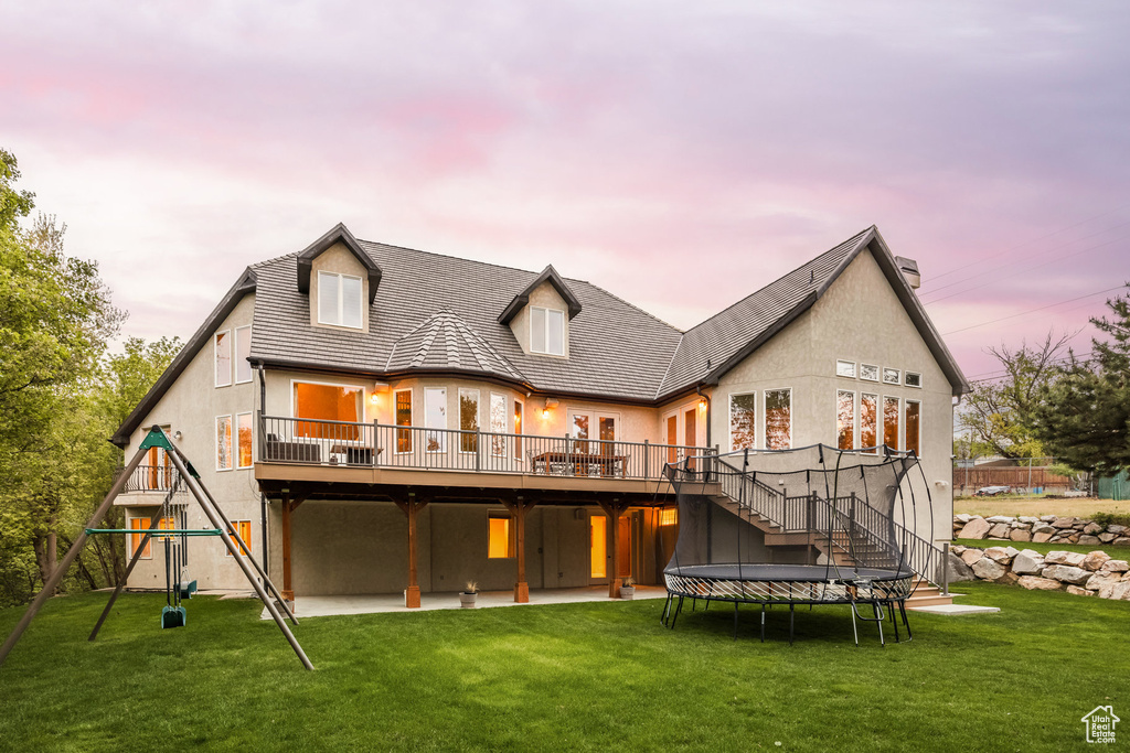 Back of house at dusk featuring a yard, stucco siding, a deck, stairway, and a playground