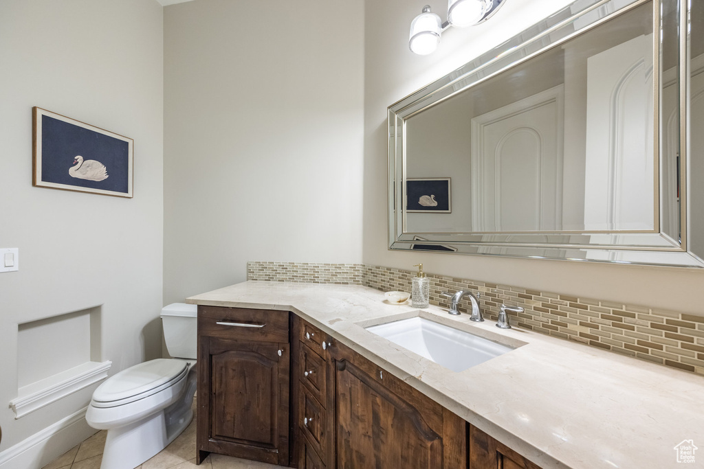 Bathroom with toilet, tile patterned flooring, vanity, and decorative backsplash