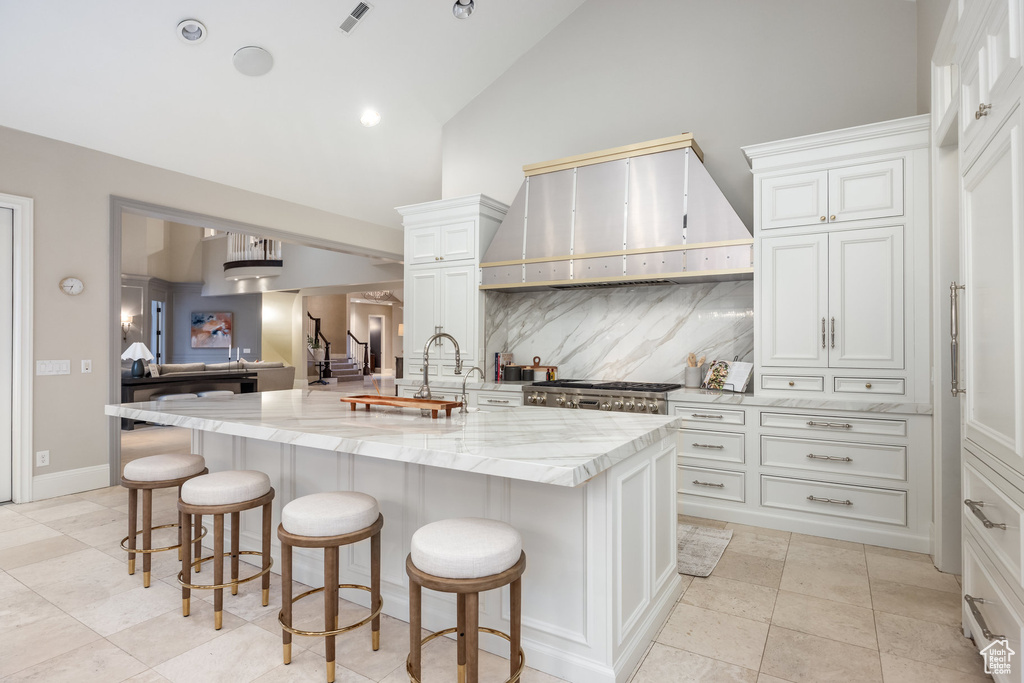 Kitchen with light stone countertops, a breakfast bar, visible vents, wall chimney exhaust hood, and backsplash