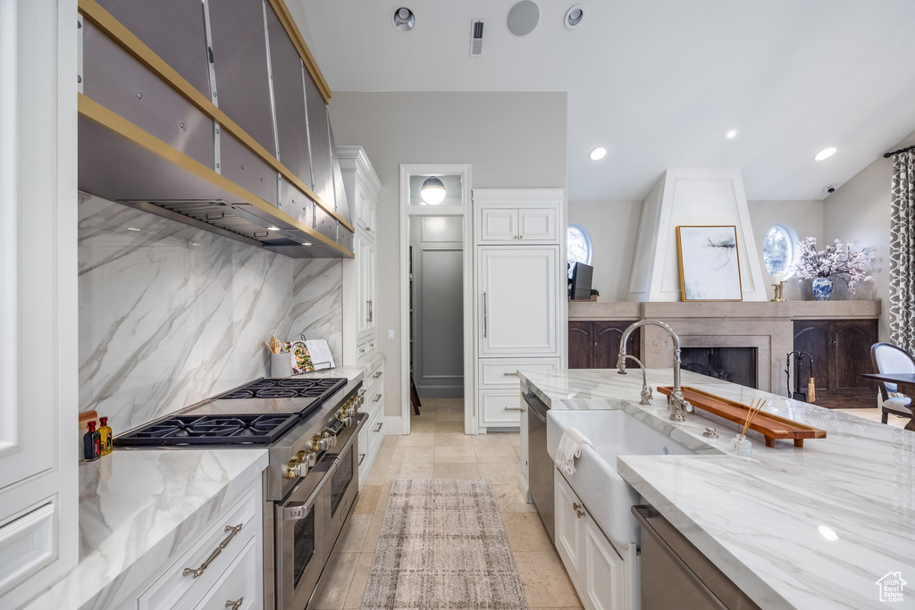 Kitchen with a sink, extractor fan, stainless steel appliances, tasteful backsplash, and a large fireplace
