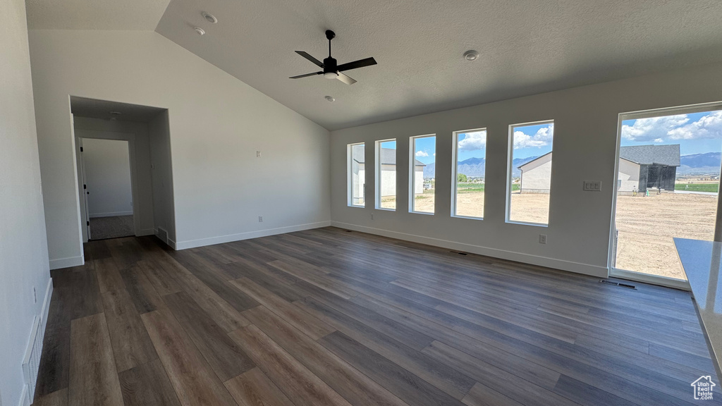 Unfurnished living room featuring dark wood finished floors, ceiling fan, baseboards, and high vaulted ceiling