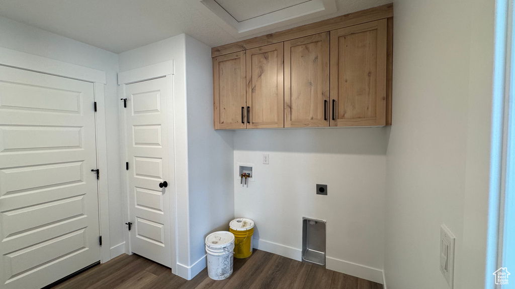Clothes washing area featuring dark wood-style floors, hookup for an electric dryer, cabinet space, hookup for a washing machine, and baseboards