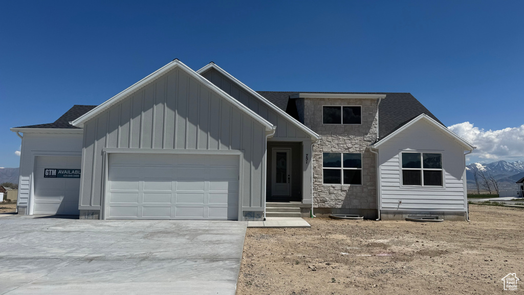 View of front of house with a garage, board and batten siding, driveway, and stone siding