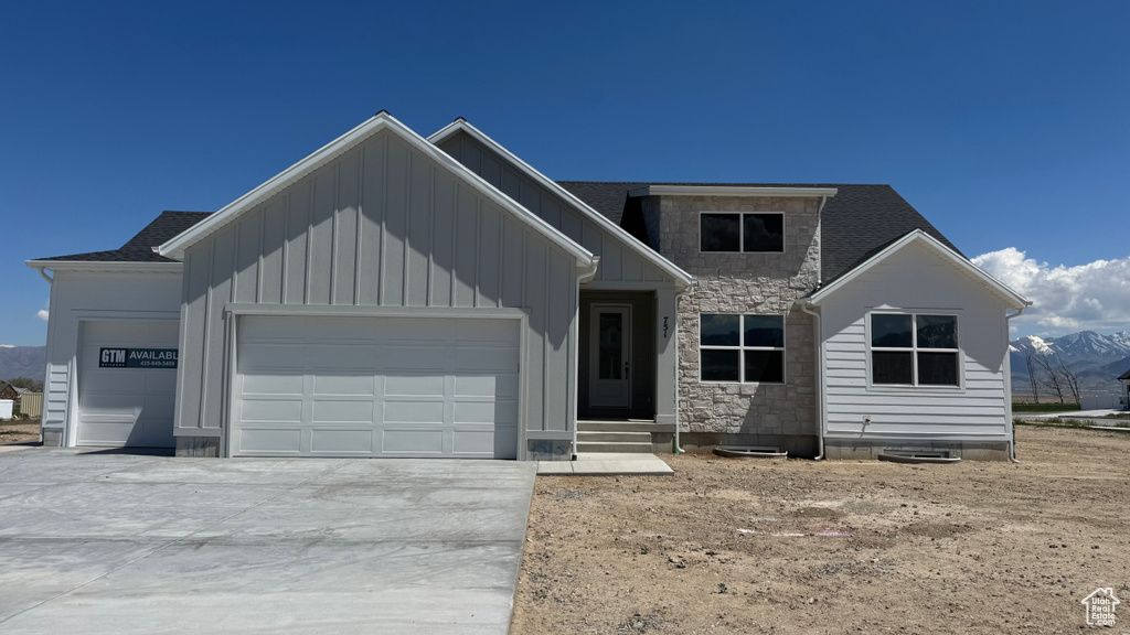 View of front facade featuring a garage, board and batten siding, concrete driveway, stone siding, and a mountain view