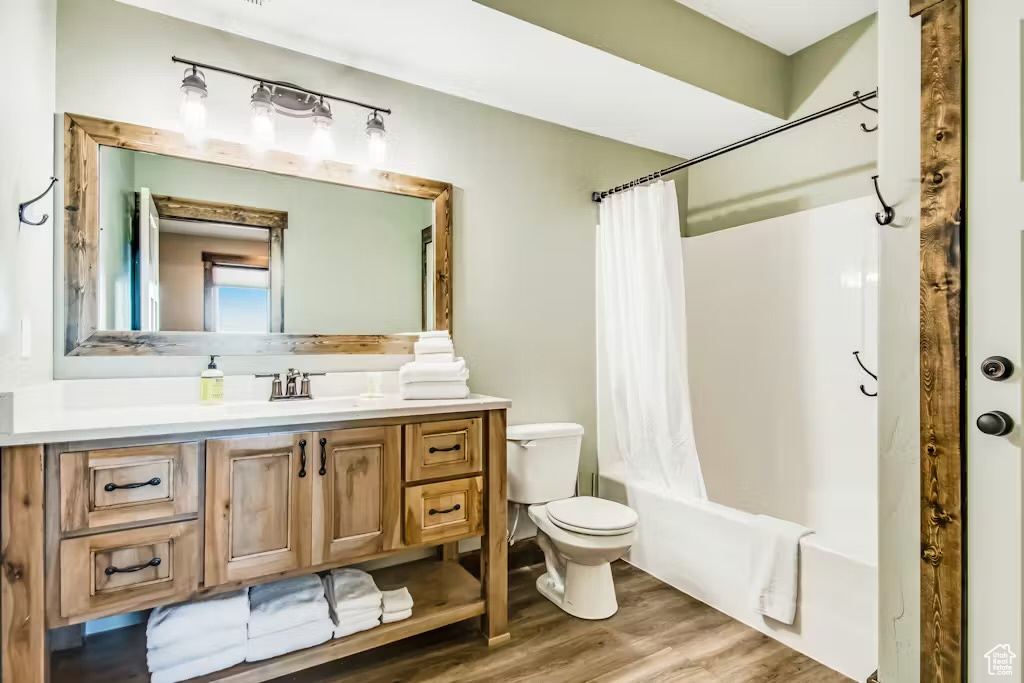 Full bath featuring shower / bath combination with curtain, toilet, wood finished floors, and vanity