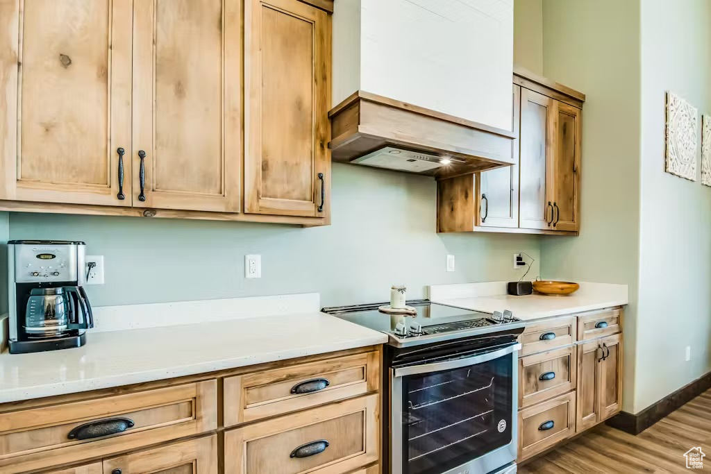 Kitchen with light countertops, premium range hood, wood finished floors, and electric range