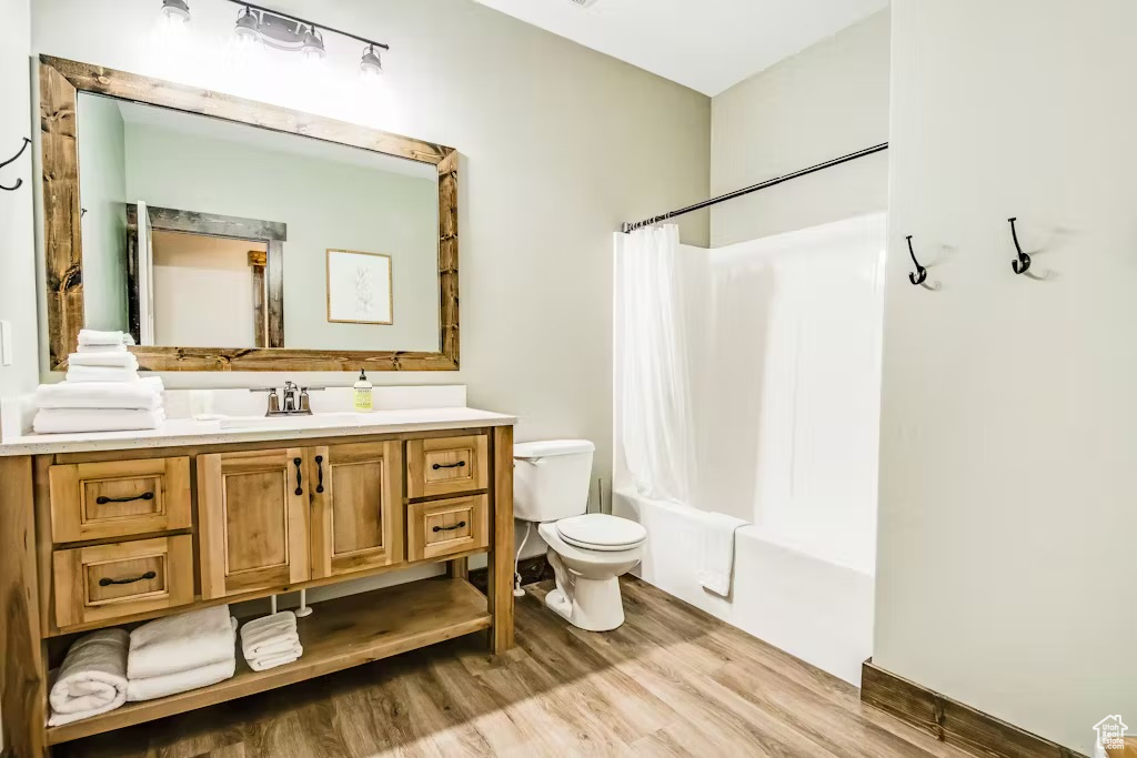Full bath featuring vanity, toilet, shower / bath combination with curtain, and wood finished floors