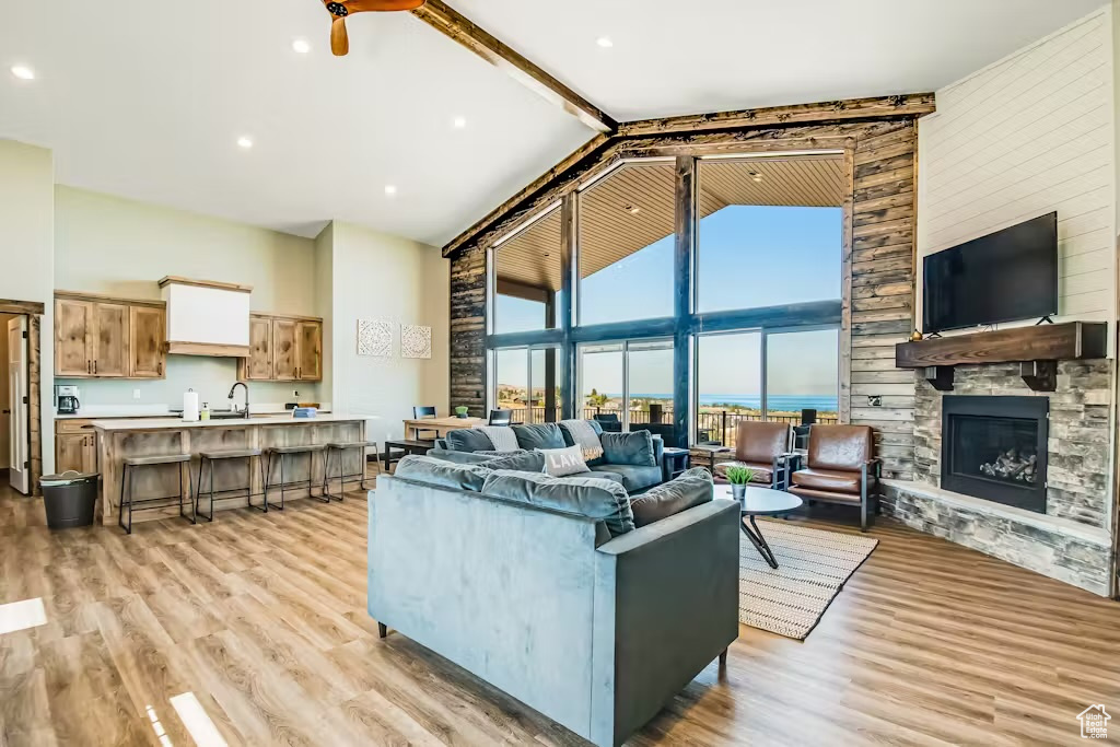 Living room featuring light wood-type flooring, beamed ceiling, a fireplace, and high vaulted ceiling