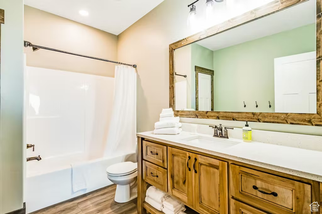 Bathroom featuring toilet, vanity, shower / bath combo, and wood finished floors
