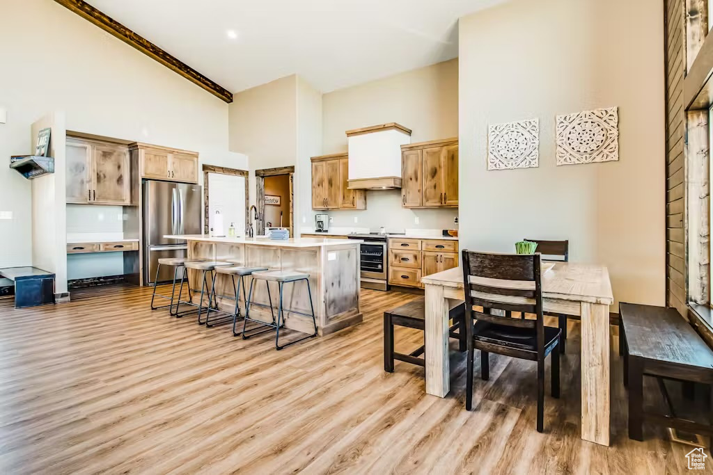 Kitchen with light wood-style flooring, a kitchen bar, light countertops, a high ceiling, and appliances with stainless steel finishes