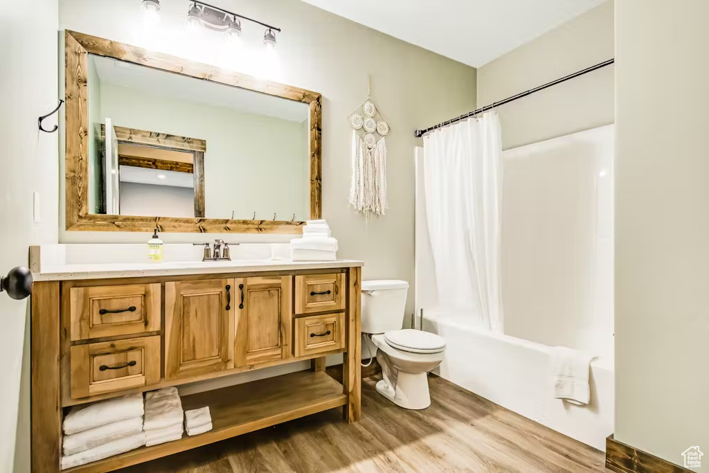 Bathroom with vanity, toilet, shower / bath combo with shower curtain, and wood finished floors