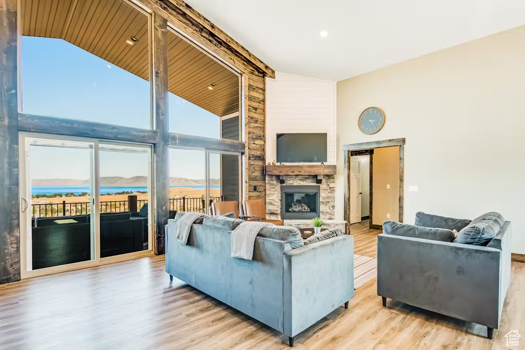 Living room featuring a stone fireplace, beam ceiling, high vaulted ceiling, and wood finished floors