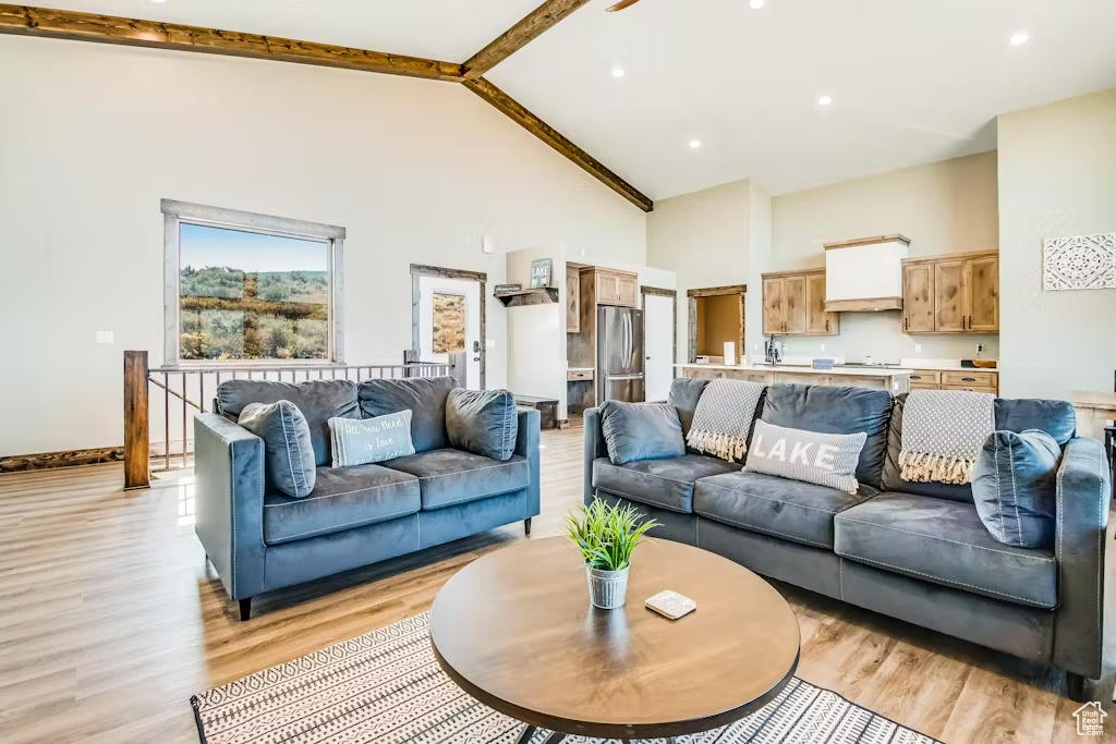 Living area featuring light wood-style floors, baseboards, beamed ceiling, and high vaulted ceiling