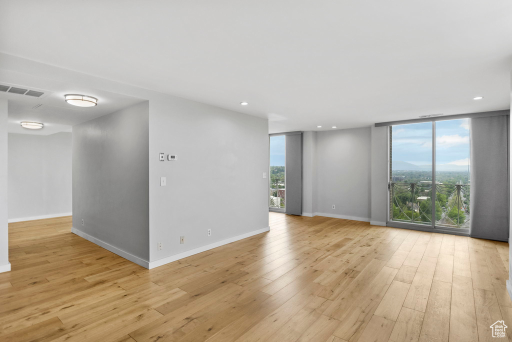 Empty room with floor to ceiling windows, recessed lighting, baseboards, and light wood-style floors