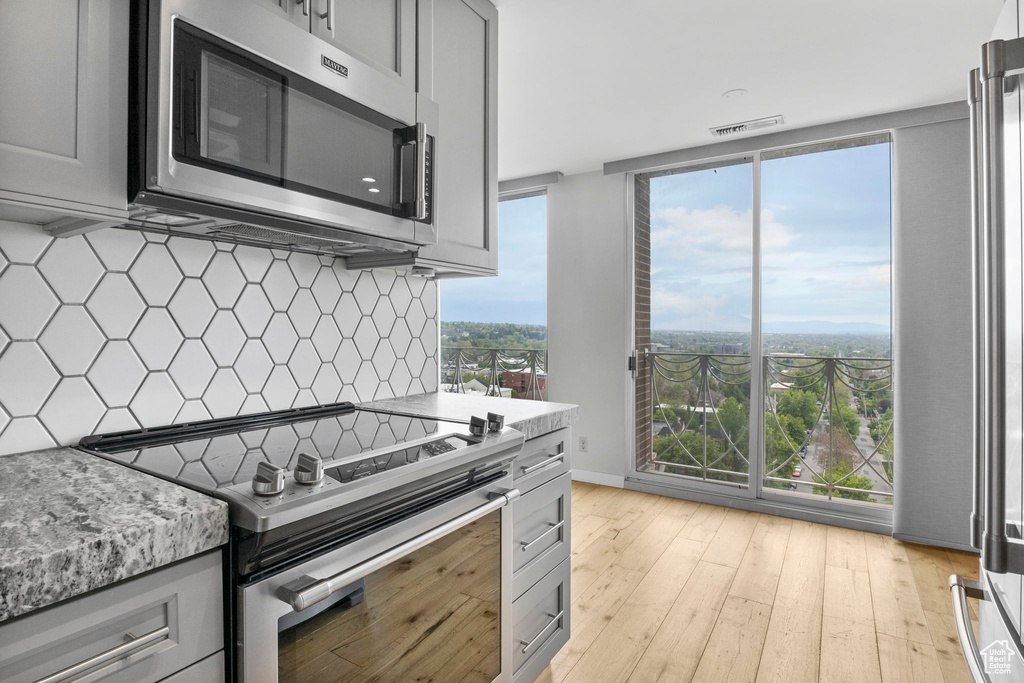 Kitchen with light wood-style flooring, gray cabinetry, backsplash, and appliances with stainless steel finishes