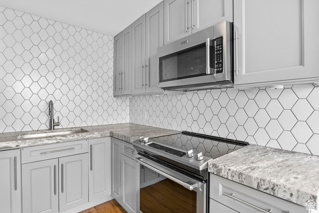 Kitchen featuring light wood-style flooring, a sink, light stone countertops, backsplash, and appliances with stainless steel finishes